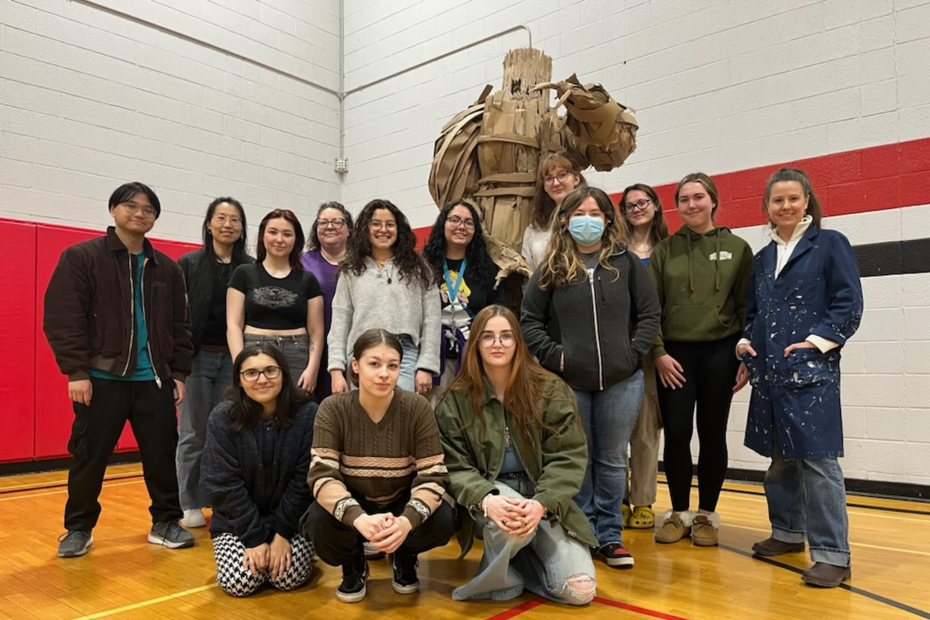 A group of first-year Fine Arts students pose with their large-scale artwork of a wood cut out creature